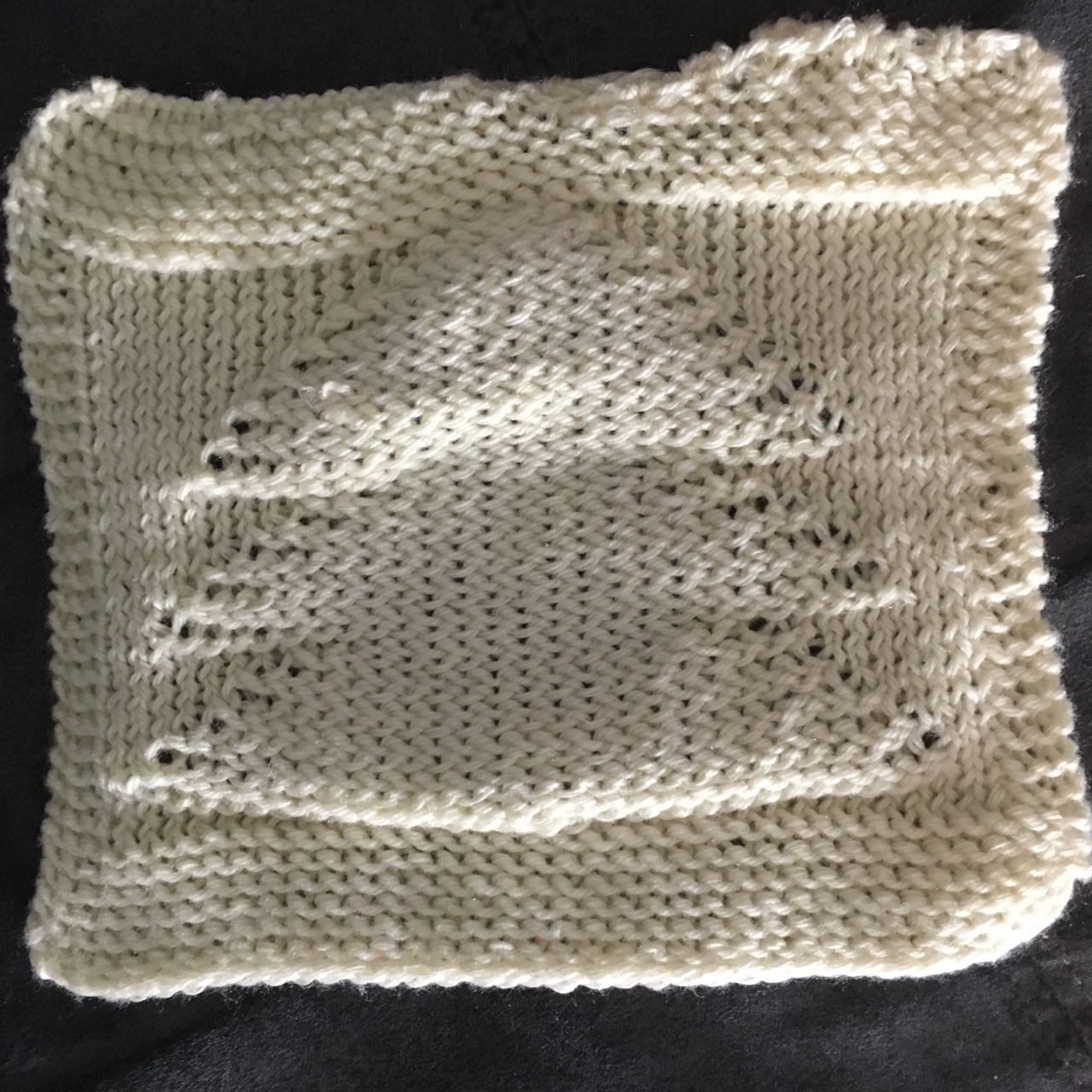 A cream colored dish cloth featuring the puffy geometric shape of a Christmas tree centered within a thick border, lays flat with the thin edge of a grey background framing the image.