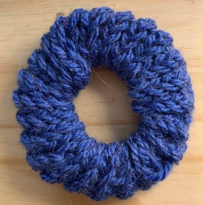Closeup of a dark blue hair scrunchie on a light wood background.