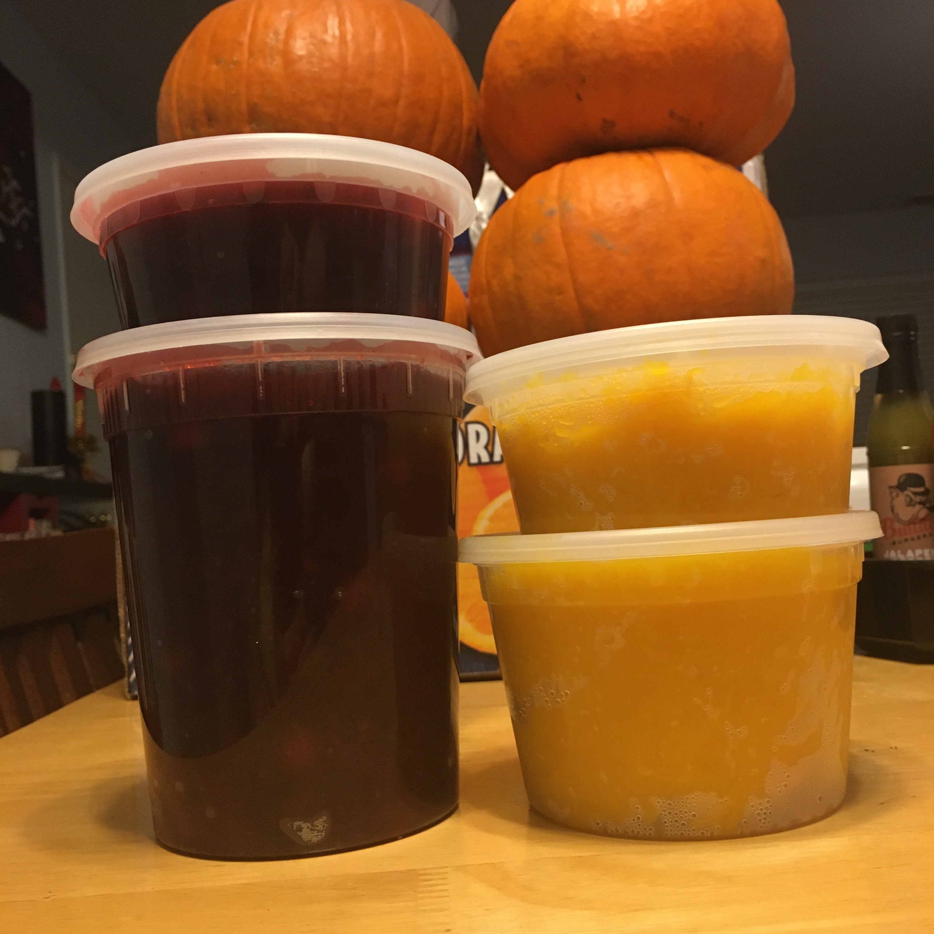 Two stacks of clear plastic food tubs filled with applebutter, left, and pumpkin puree, right. Fresh sugar pumpkins are seen stacked in the background.
