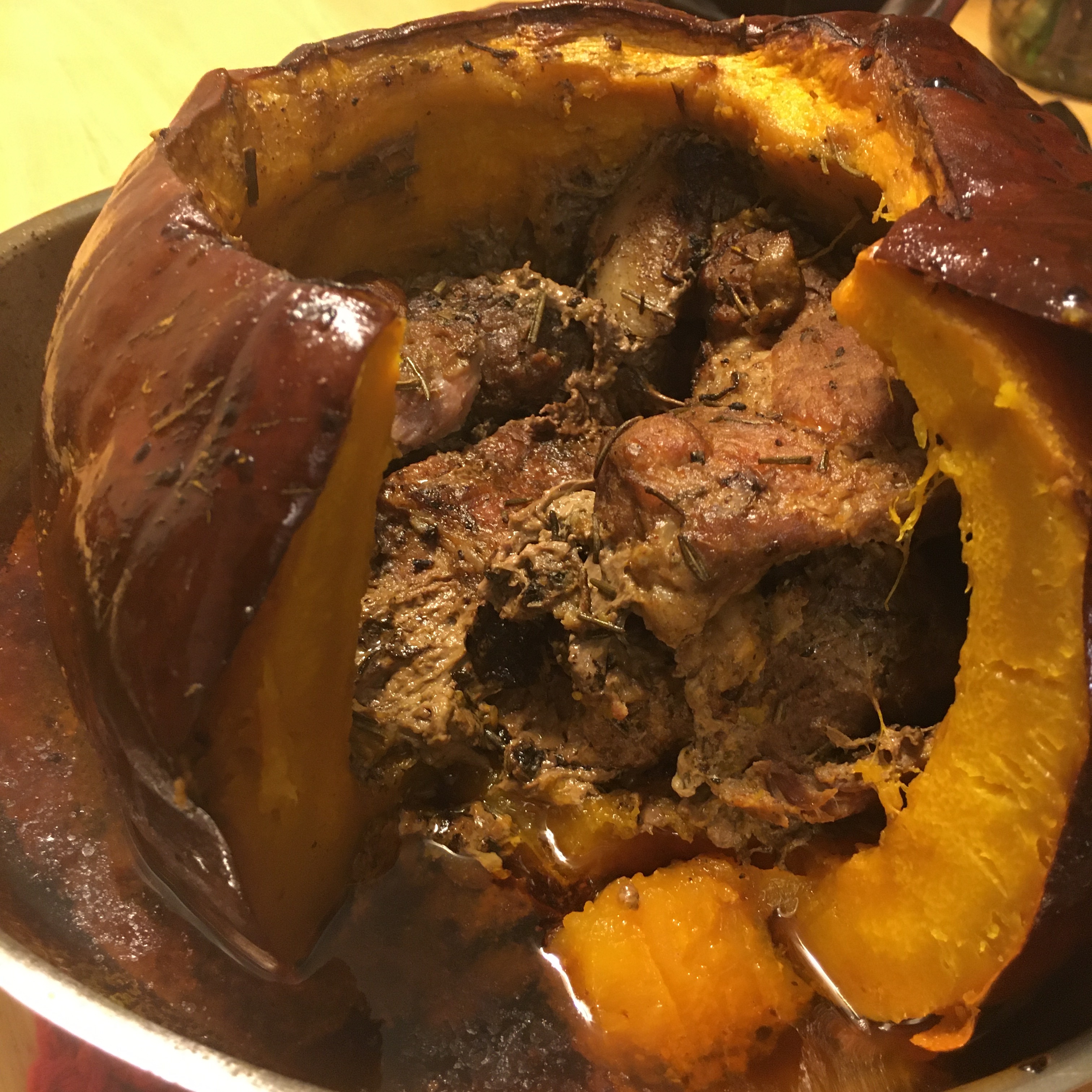 A whole pumpkin, without its top, browned from extended roasting, and oily from being brushed with it’s roasting juices, rests in a baking dish with a wedge cut out of the front, pumpkin laying out flat revealing roast pork inside.