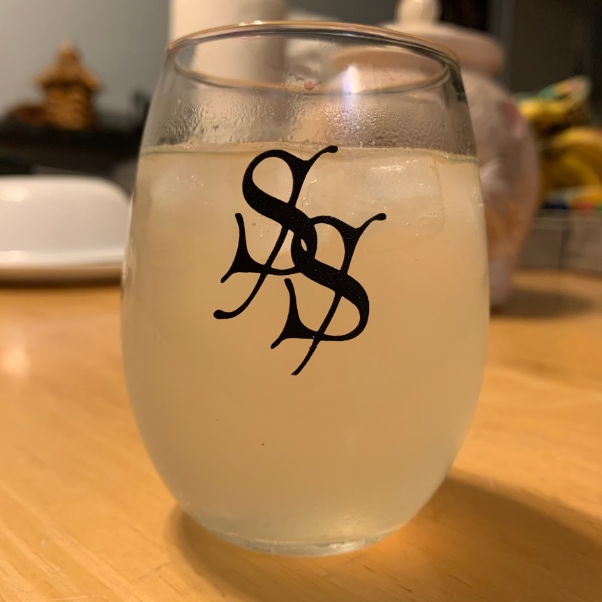 Close up of a stemless wine glass with two stylized Ss interlocking on the front, filled with ice and pale yellow liquid.