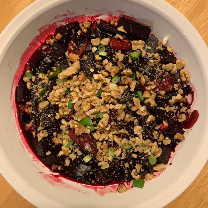 Aerial POV of chopped beets in a glazey sauce, topped with chopped green onions and chopped walnuts.