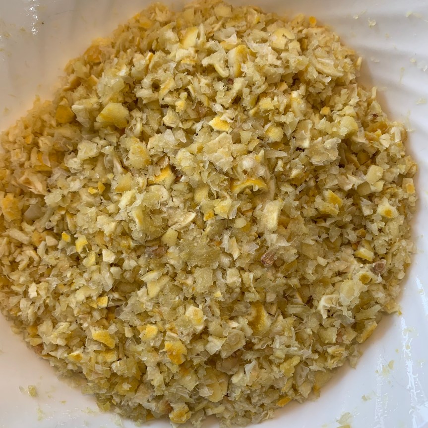 Aerial POV of coarsely food processed lemon rinds in a deli food storage tub.