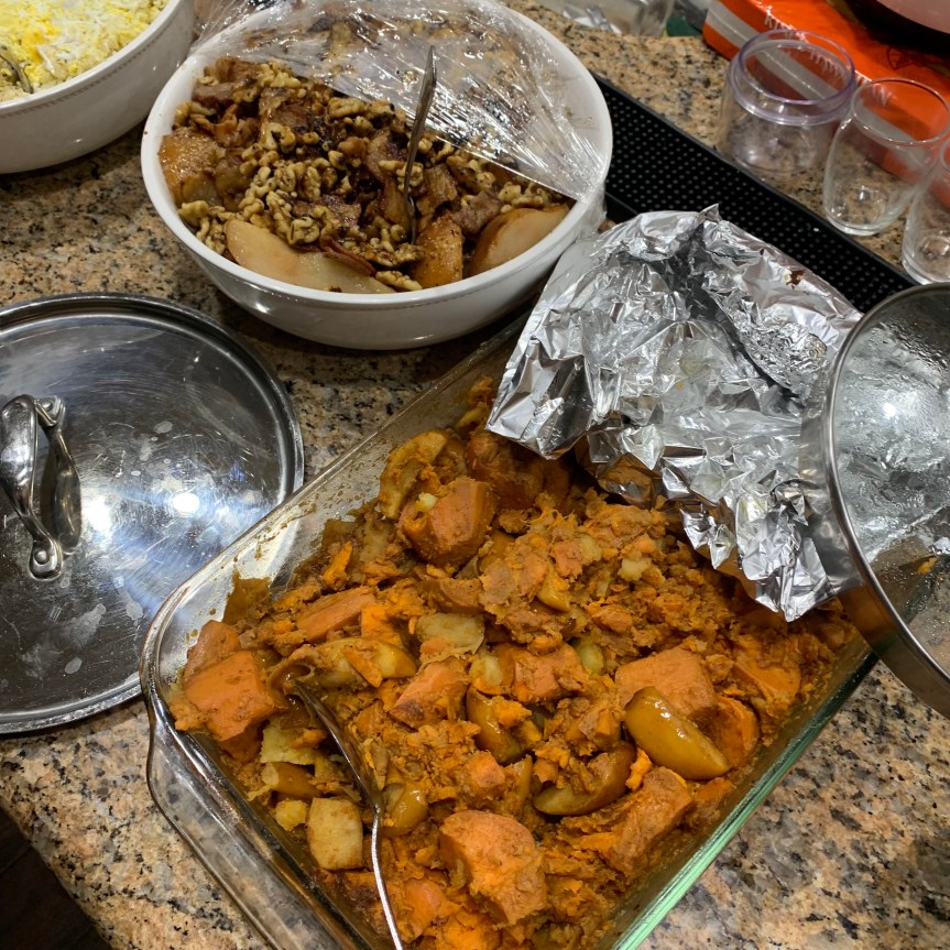 Angled aerial POV of two dishes in a home Thanksgiving buffet style dinner, a 9X11 glass baking dish right and front full of roasted sweet potato and apple mash, a large bowl, left and back slightly, full of sauteed pears with bacon and mustard vinaigrette.